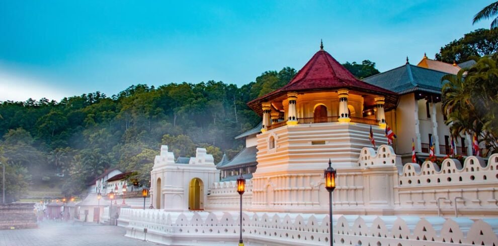 Aerial view of the picturesque city of Kandy surrounded by lush green hills, with the Temple of the Tooth Relic and Kandy Lake prominent in the center.